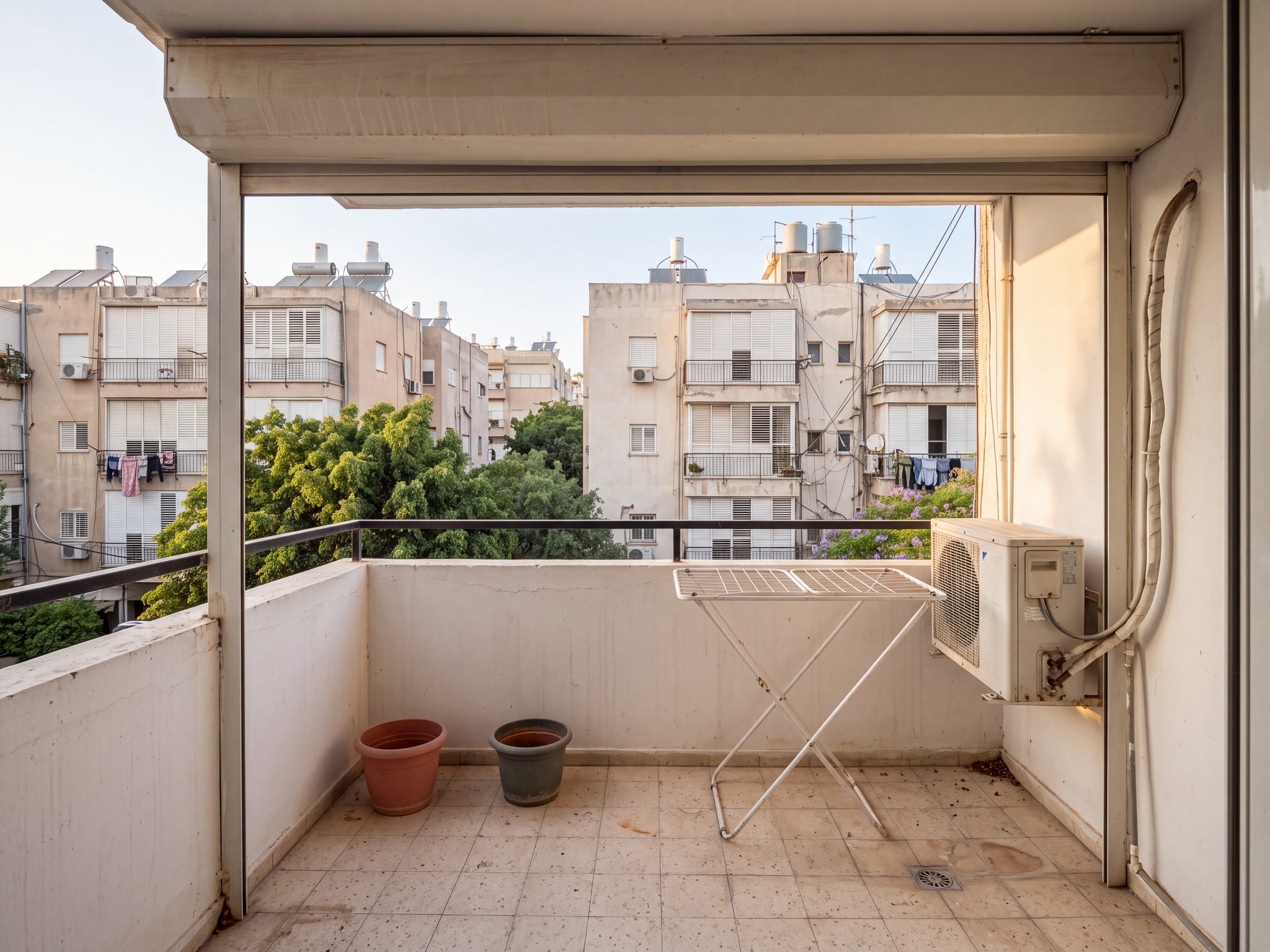 לפני, הדמיה: מרפסת צרה בבניין ישן עם מתקן ייבוש כביסה, עציצים ריקים ומזגן